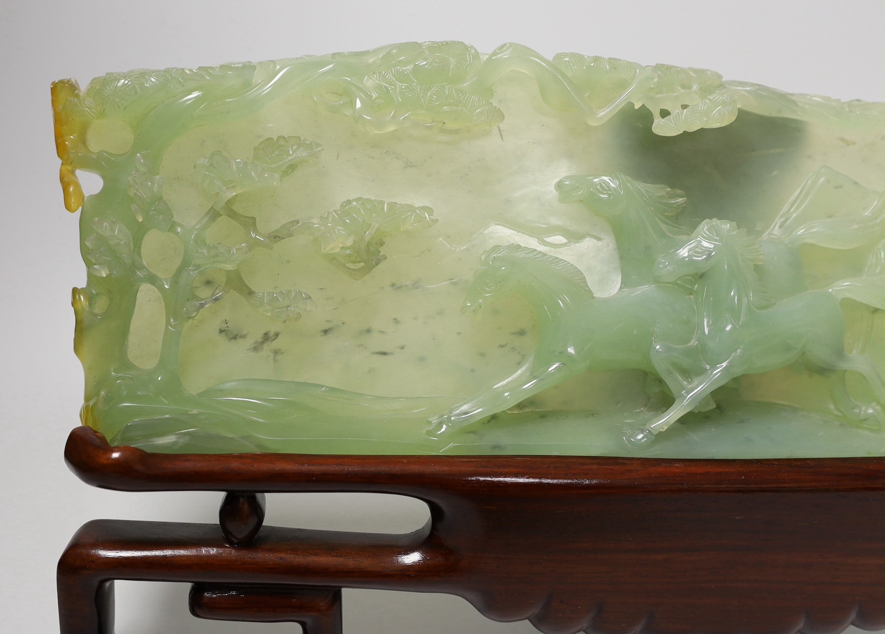 A large Chinese bowenite jade plaque of galloping horses, wood stand, 40cm wide